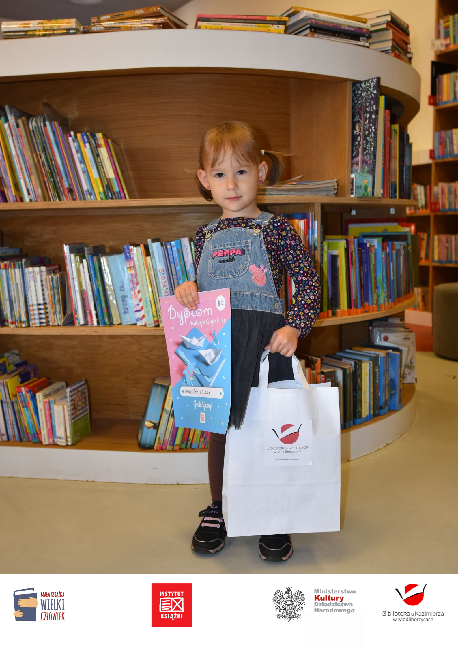 Na zdjęciu mała dziewczynka, w niebieskiej sukience o imieniu Marcelina.  Marcelinka uzbierała już 10 naklejek na Karcie Małego Czytelnika, odebrała dyplom oraz mały upominek i nadal z chęcią nas odwiedza i wypożycza książki. Macerlina btrała udział w projekcie "Mała książka - wielki człowek" realizowany przez Instytut Książki w Krakowie. 